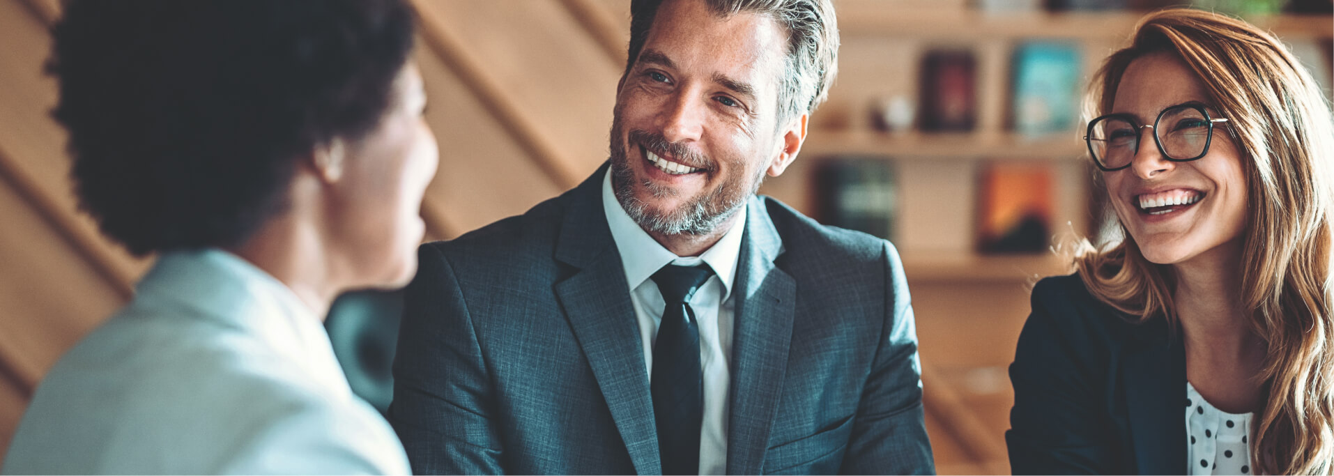 Drei lächelnde Personen unterhalten sich im Businessoutfit.